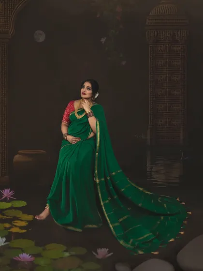 A beautiful portrait of a mother-to-be in a rich green saree, seated gracefully amidst a lotus pond setting. The composition and soft lighting are designed to create a tranquil and elegant mood, reminiscent of classical Indian paintings.