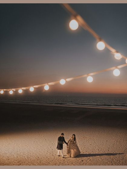 A wide shot of the couple on the beach under a string of lights as dusk settles. It's a truly cinematic and romantic moment.