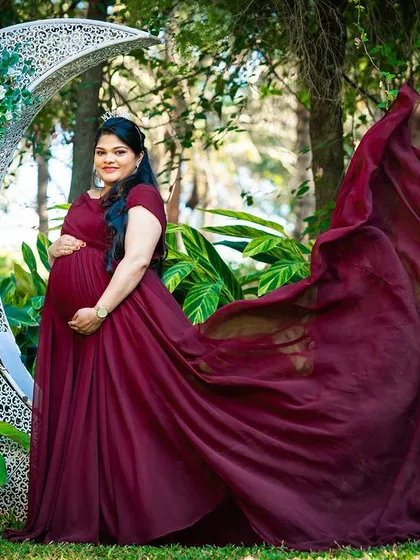 A solo maternity portrait with a flowing maroon gown by the crescent moon prop.