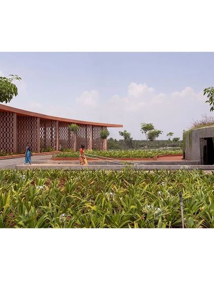 Local residents walk through the landscaped grounds of the memorial. The design uses a curved brick jali wall to create a gentle boundary, while the pathways are integrated with native plantings, making the complex feel like a natural extension of its rural surroundings.