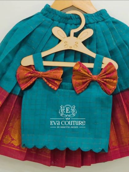 A modern and cute top and skirt set for a toddler. The teal top has adorable pattu bows on the shoulders, and the pleated skirt has a traditional pink and gold border.