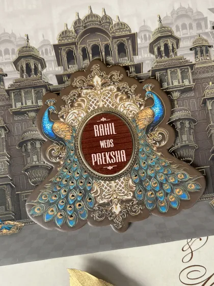 A close-up of the central motif, where two vibrant peacocks frame a wooden-finish nameplate, blending rustic texture with royal imagery.