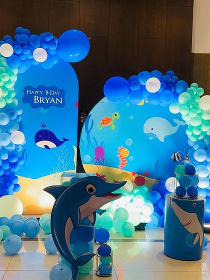 An adorable underwater theme party featuring whales, dolphins, and other sea creatures against a blue backdrop with balloon arches mimicking ocean waves.
