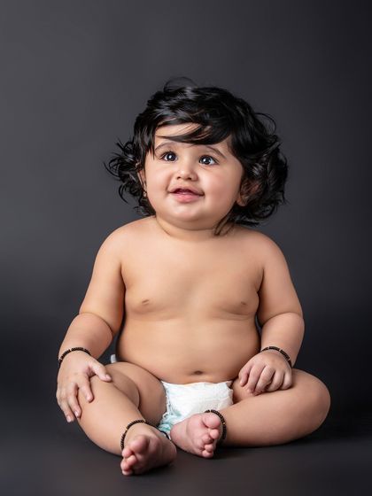 A simple and beautiful portrait of a baby in a diaper against a dark background, highlighting those adorable baby rolls.