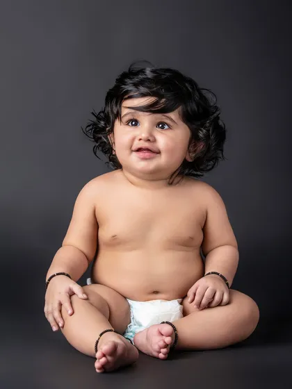 A simple and beautiful portrait of a baby in a diaper against a dark background, highlighting those adorable baby rolls.