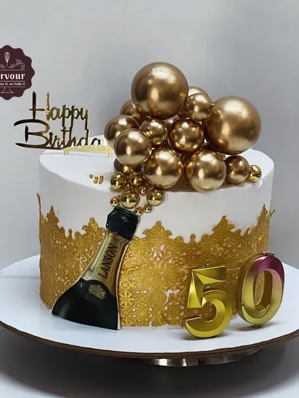 A glamorous 50th birthday cake with a champagne theme. This chocolate mousse cake is decorated with a gold lace effect, golden spheres, and a mini champagne bottle.