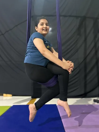 A happy student takes a moment to smile while sitting comfortably in the aerial hammock, a great starting point for beginners.