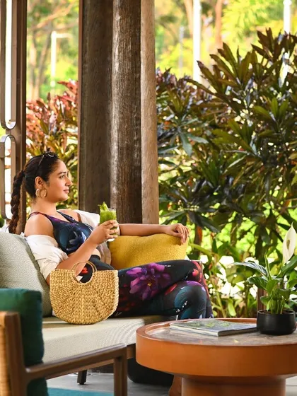 A guest relaxes on a comfortable sofa in one of our open-air lounges, surrounded by lush plants. These spaces are designed for quiet contemplation and relaxation.