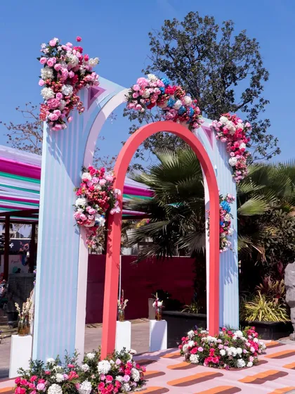 The entrance to the 'Art in the City' carnival, with layered arches in pastel stripes and bold coral, adorned with beautiful floral arrangements.