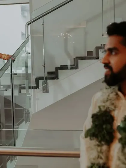 A "first look" style shot on a modern staircase, capturing the groom's reaction as he sees his bride in her stunning South Indian wedding attire.