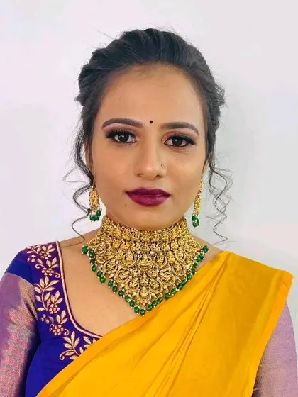 A model wearing a traditional South Indian temple jewellery choker with green beads, paired with a yellow and blue silk saree.