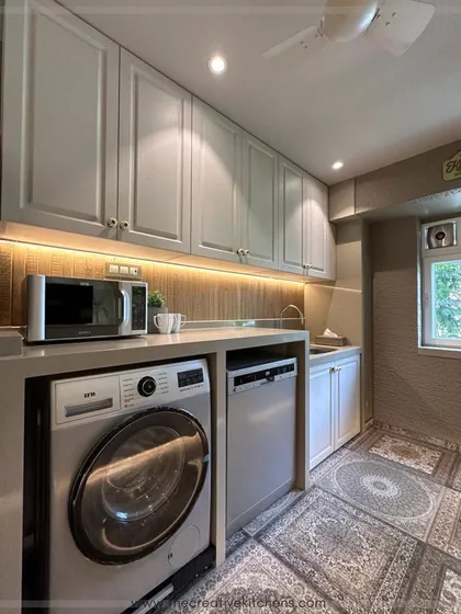 Even utility spaces are designed with care. This section of the kitchen neatly houses the washing machine and dishwasher under the counter, maintaining a clean look while keeping appliances easily accessible.