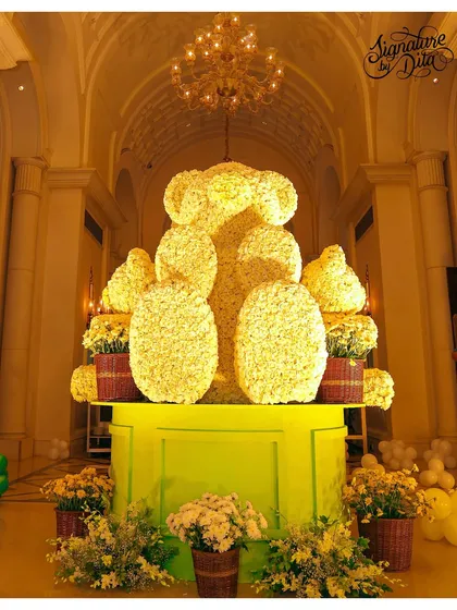 Another angle of the magnificent floral teddy bear sculpture, showing its impressive scale under the grand chandelier of the venue.