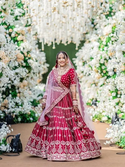 A bride's look is complete only when seen with her full attire and the beautiful decor of her special day. This stunning shot captures the entire vision, from the intricate lehenga and flawless makeup to the grand floral archway.