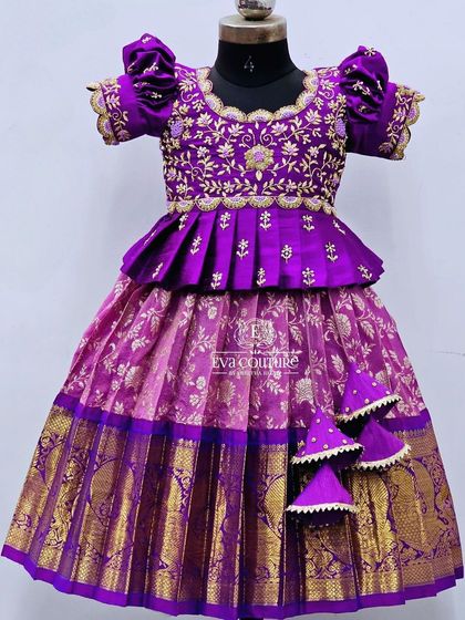 A rich purple and pink Kanchi Pattu lehenga. The blouse features a pleated peplum and intricate gold embroidery.
