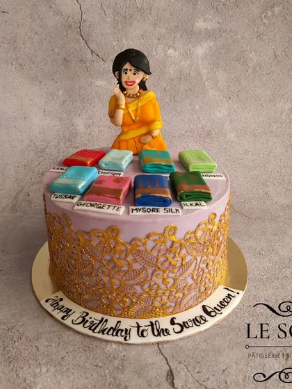I love bringing your passions to life, like with this "Saree Queen" cake. It features a hand-sculpted figurine and a collection of miniature, detailed 3D sarees in various styles like Mysore Silk and Georgette, all sitting on a cake with an intricate golden lace design.