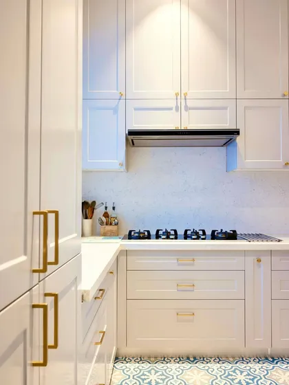 A classic all-white kitchen with shaker-style cabinets and elegant brass handles. The patterned floor tiles add a touch of personality and prevent the space from feeling too sterile.