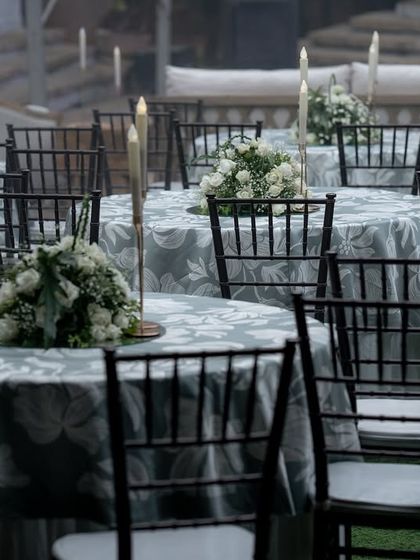 Elegant round table seating arranged on the lawn for a Sangeet evening, with floral centerpieces and Chiavari chairs.
