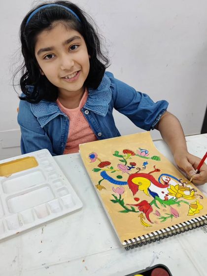 A young student learns a traditional Indian folk art style, carefully painting vibrant, stylized birds and flowers.