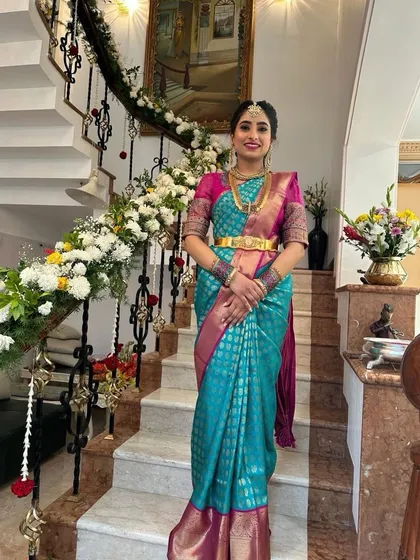A full-length view of the bride on the grand staircase, showcasing the beautiful drape and rich colors of her blue and pink Kanchipuram silk saree.