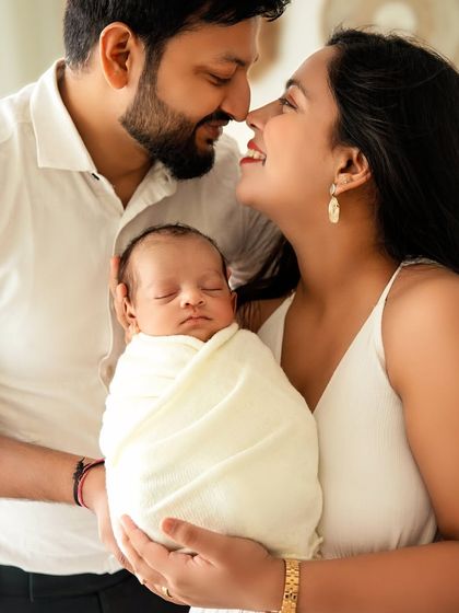 A joyful family portrait, with the parents smiling at each other while holding their precious baby.