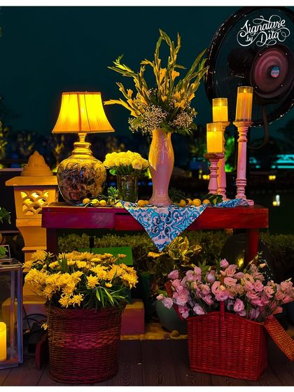 A beautifully styled corner vignette featuring a mix of fresh flowers, lanterns, candles, and a table lamp, creating a warm and inviting pocket of light and color.