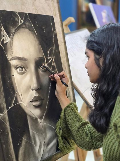 An intimate shot of the artist adding fine details to the eye in her charcoal portrait, a critical step in bringing the subject to life.
