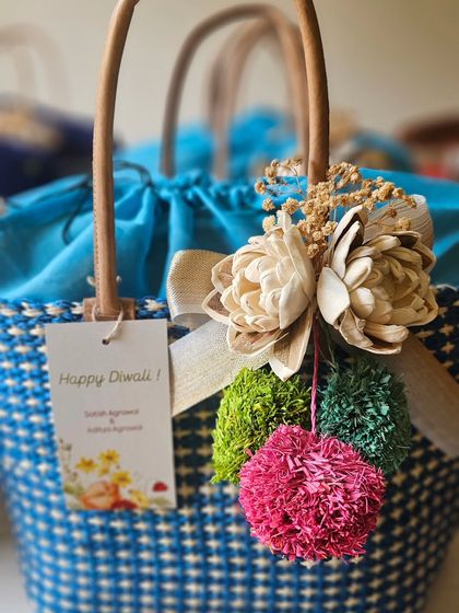 A "Happy Diwali" tag adds a festive touch to this beautiful blue and white raffia basket. The colorful pom-poms and dried flowers make it a cheerful and sustainable gift.