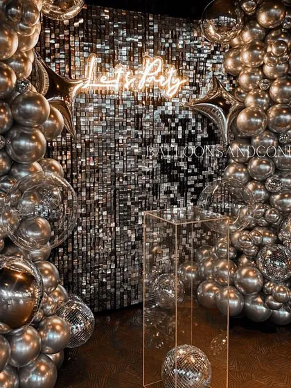 A closer look at the silver 'Let's Party' decor, focusing on how the neon sign and balloons interact with the reflective shimmer wall.