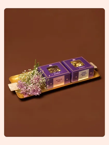 Two beautifully packaged sweet boxes on a golden tray, styled with fresh flowers for a Rakhi special. This image focuses on the elegance and gift-worthiness of the product.