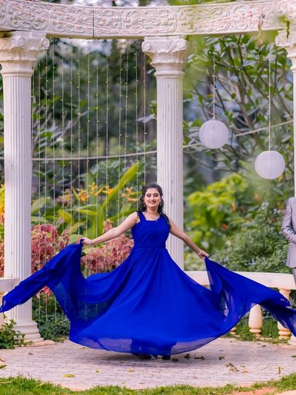 A woman in a flowing blue dress twirls in front of a white colonnade in the garden, creating a beautiful and dynamic shot.