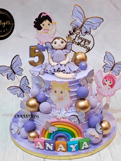 A dreamy two-tier doll and butterfly cake for a fifth birthday. This blueberry cake is designed in a beautiful lavender color, with a doll topper, a rainbow, and fluttering butterflies.