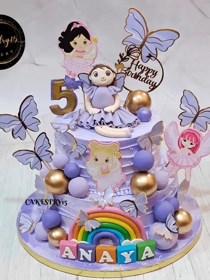 A dreamy two-tier doll and butterfly cake for a fifth birthday. This blueberry cake is designed in a beautiful lavender color, with a doll topper, a rainbow, and fluttering butterflies.