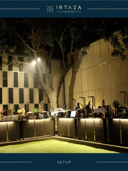 A wide-angle view of an expansive outdoor buffet setup against a modern architectural backdrop. The under-counter lighting adds a dramatic effect, showcasing the scale and sophistication I bring to large-scale events.