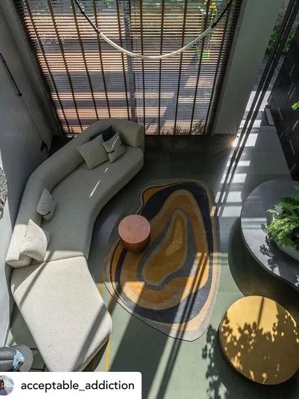 An aerial view of a stylishly furnished lounge area next to an indoor courtyard. The organic shapes of the rug and sofa echo the natural forms of the plants, creating a cohesive design language.