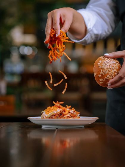 Assembling the Hickory-Smoked Pulled Pork Burger, with a generous topping of crispy fried onions.