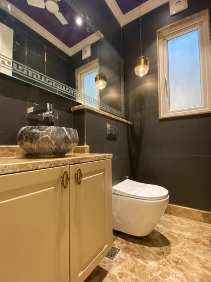 A bold and beautiful bathroom design. The dark walls and purple ceiling are offset by a unique stone-carved sink and elegant pendant lighting.