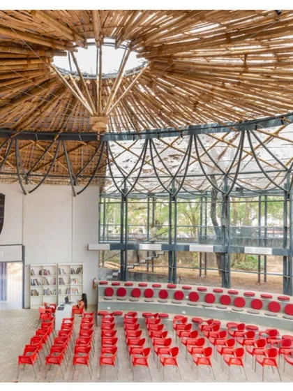 An interior view of the Koodaaram Pavilion in Kochi, a performance space designed for the Kochi-Muziris Biennale. The intricate bamboo canopy and steel structure create a space that is both grand and light, with tiered seating that fosters a sense of community among the audience.