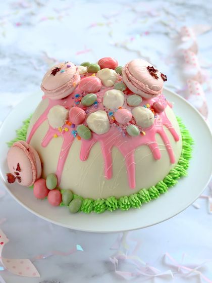 The White Chocolate Dome Pinata Cake before it's smashed, showing the beautiful pink drip and macaron decorations.
