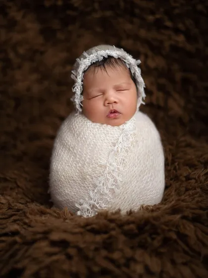 Perfectly swaddled and sleeping soundly. This classic newborn portrait, known as the potato sack pose, highlights the baby's peaceful features while ensuring they are snug, safe, and comfortable.