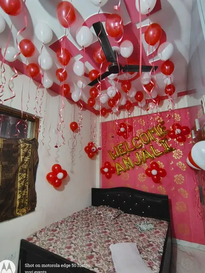 A simple "Welcome Anjali" room decoration with red and white balloons on the ceiling and foil letters on the wall.