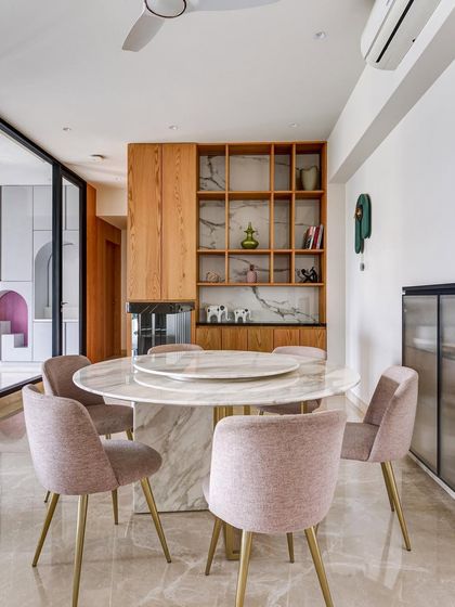 This dining area features clever storage integrated into a wood and marble unit. The soft pink chairs add a touch of warmth and color to the elegant space, which is designed to be both beautiful and highly functional.