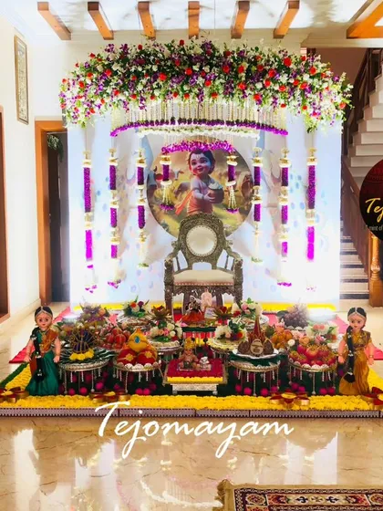 An intimate at-home baby shower decoration. The setup includes a portrait of baby Krishna, silver lamps, and a beautiful arrangement of traditional plates, creating a warm and divine atmosphere.