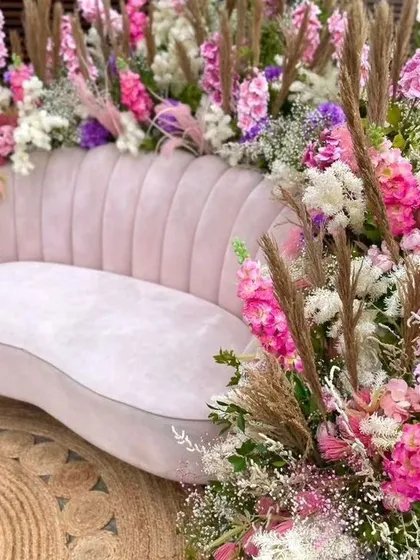 A close-up of a plush pink sofa surrounded by a lavish arrangement of colorful flowers. This makes for a beautiful and comfortable seating spot for the bride during the Mehendi ceremony.