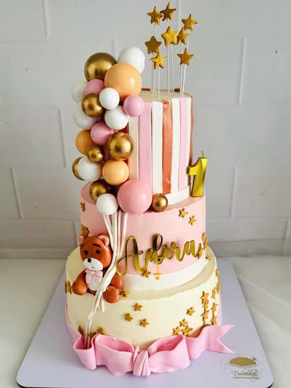 A grand three-tier cake for a first birthday celebration. This design features a cute teddy bear, a cascade of balloons, and sparkling gold stars for a truly festive look.