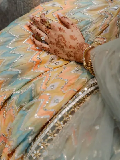 A close-up on the intricate details. This shot highlights the beautiful gota patti work on the bride's lehenga and the delicate henna on her hand, small details that tell a larger story of tradition and style.