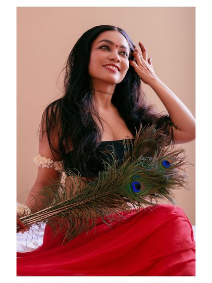 An artistic portrait featuring a peacock feather. The composition and the subject's expression create a sense of connection to nature and a quiet, meditative mood.