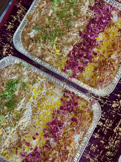 Two large foil trays filled with my signature biryani, garnished with saffron rice, fried onions, and rose petals, ready for a large event.