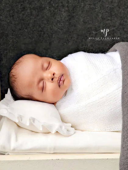 The baby is tucked in with a grey blanket in the miniature bed.