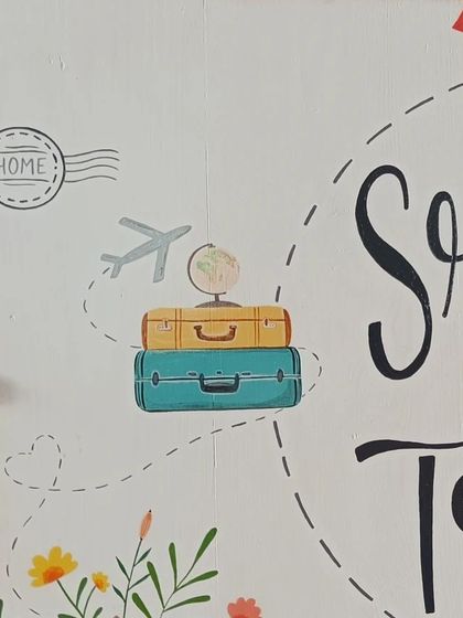 Detail shot of the travel-themed name board, showing the hand-painted suitcases, globe, and airplane, capturing the couple's wanderlust spirit.